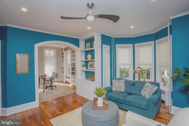 living area with crown molding, radiator heating unit, hardwood / wood-style flooring, ceiling fan, and arched walkways