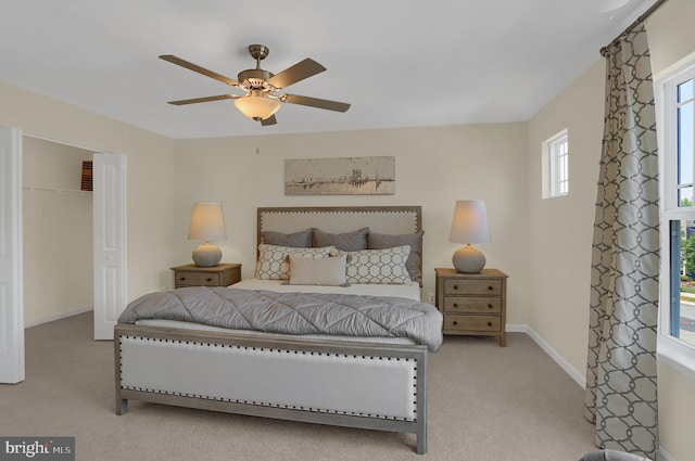 bedroom featuring light carpet, ceiling fan, a closet, and a walk in closet