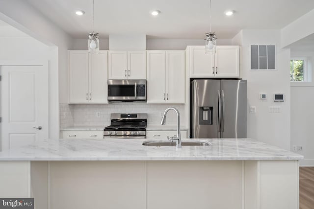 kitchen with a kitchen island with sink, stainless steel appliances, sink, and white cabinetry