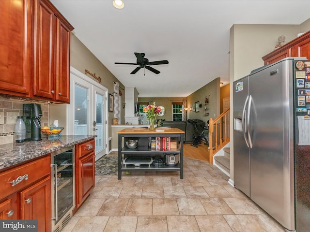 kitchen featuring ceiling fan, stainless steel fridge, beverage cooler, backsplash, and dark stone counters