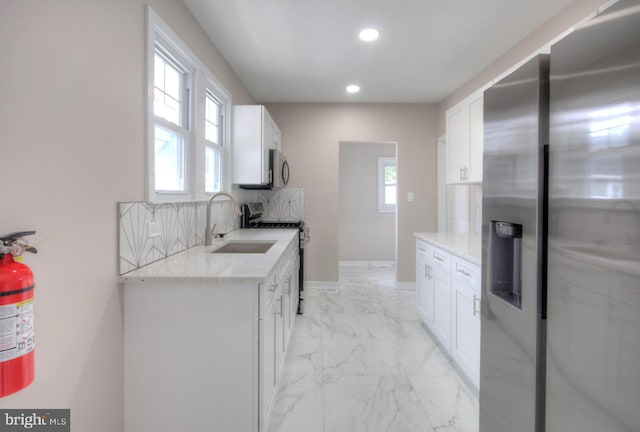 kitchen with light stone countertops, backsplash, white cabinets, and appliances with stainless steel finishes