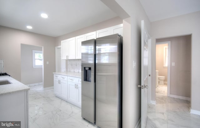 kitchen with light stone counters, white cabinets, backsplash, and stainless steel fridge with ice dispenser