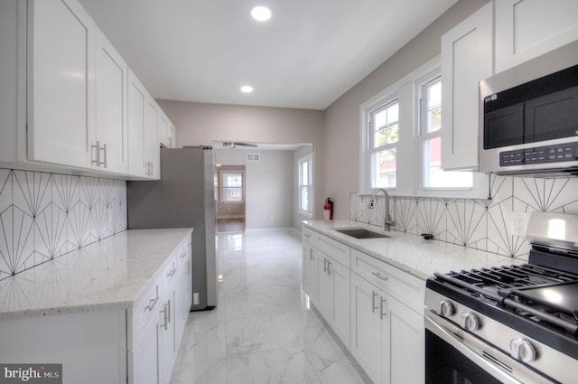 kitchen with stainless steel appliances, decorative backsplash, light stone counters, and white cabinetry