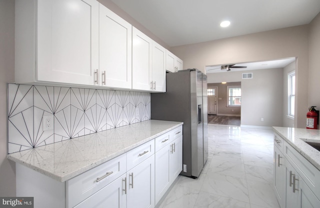 kitchen with ceiling fan, light stone counters, backsplash, stainless steel fridge with ice dispenser, and white cabinetry