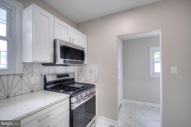 kitchen with light stone counters, white cabinets, appliances with stainless steel finishes, and tasteful backsplash