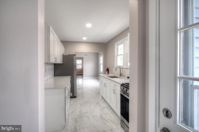 kitchen with white cabinets, appliances with stainless steel finishes, sink, and light stone counters