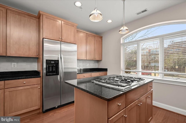 kitchen with tasteful backsplash, dark stone countertops, appliances with stainless steel finishes, and light hardwood / wood-style flooring