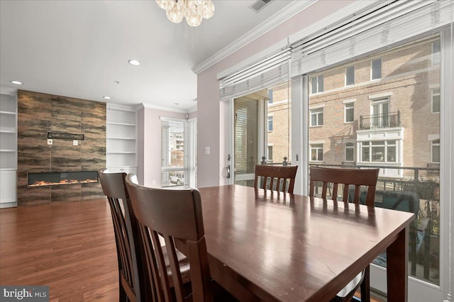 dining room with ornamental molding, hardwood / wood-style flooring, built in features, and a large fireplace