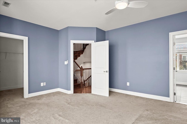 unfurnished bedroom featuring a closet, light colored carpet, a walk in closet, and ceiling fan