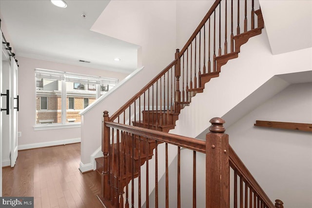 stairway featuring wood-type flooring, ornamental molding, and a barn door