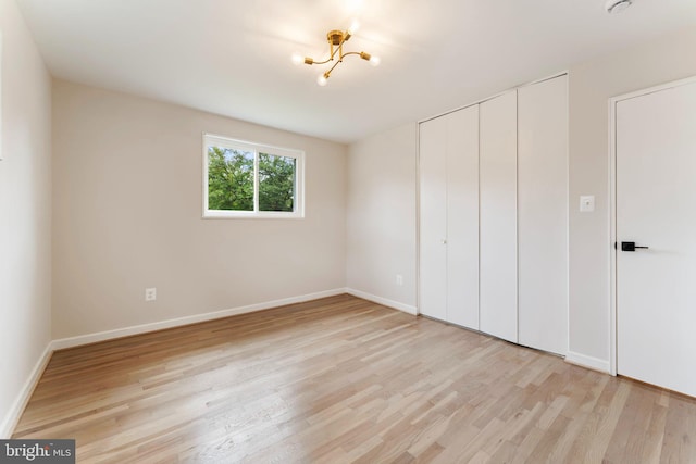 unfurnished bedroom featuring an inviting chandelier, light hardwood / wood-style flooring, and a closet