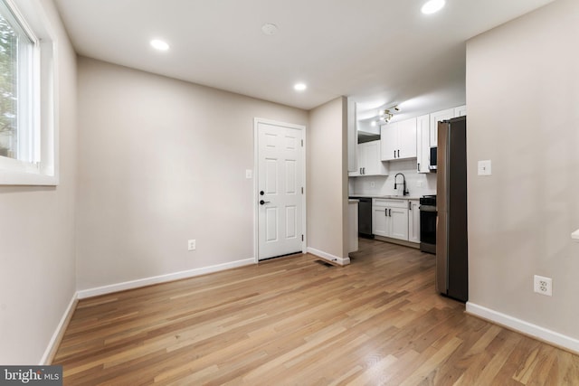 kitchen with appliances with stainless steel finishes, white cabinets, sink, and light wood-type flooring