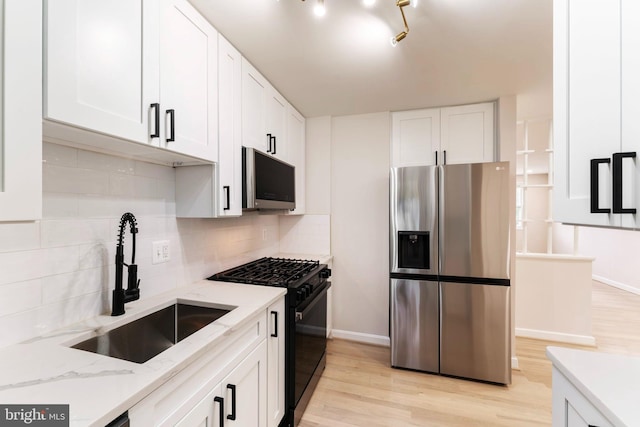 kitchen with light hardwood / wood-style flooring, stainless steel appliances, sink, light stone countertops, and white cabinetry