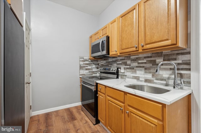 kitchen with backsplash, appliances with stainless steel finishes, light wood-type flooring, and sink