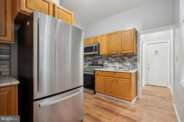 kitchen with stainless steel appliances, light wood-type flooring, sink, and tasteful backsplash