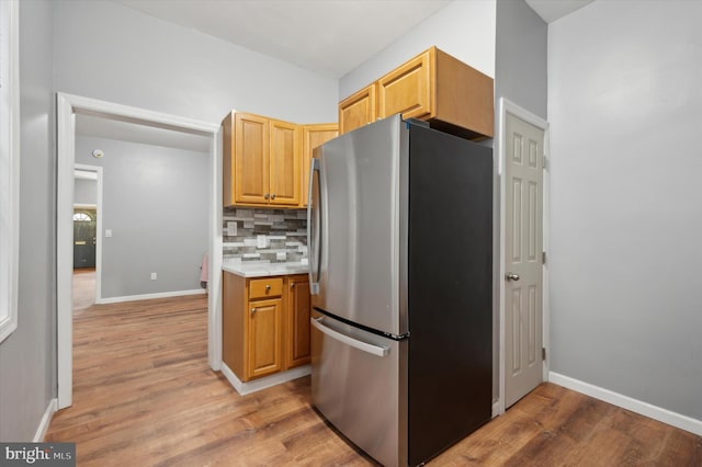 kitchen featuring light wood-type flooring, decorative backsplash, and stainless steel refrigerator