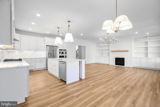 kitchen featuring a large fireplace, stainless steel appliances, a kitchen island with sink, decorative light fixtures, and white cabinetry