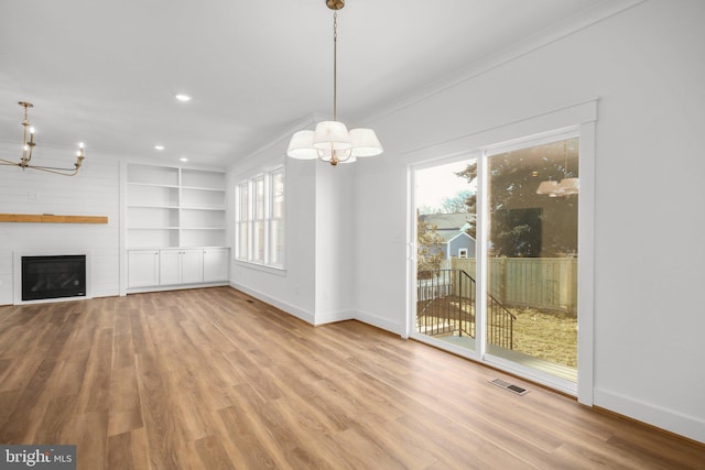 unfurnished living room with crown molding, a fireplace, light wood-type flooring, and a notable chandelier