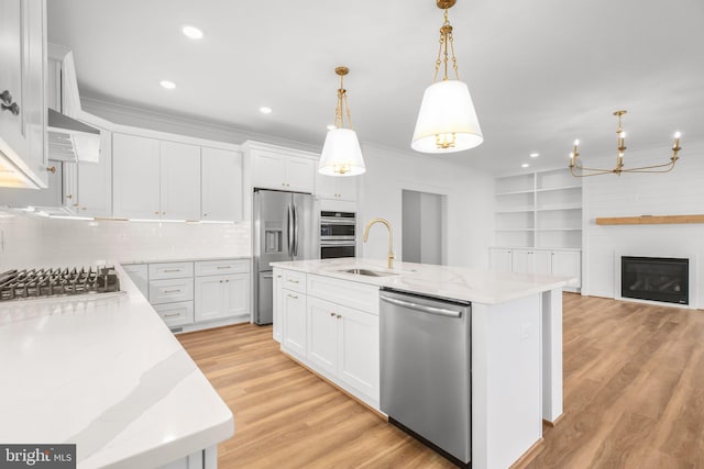 kitchen with light stone counters, decorative light fixtures, a kitchen island with sink, white cabinets, and appliances with stainless steel finishes