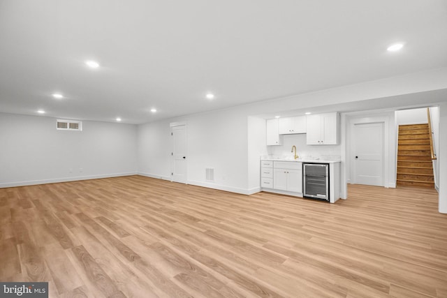 unfurnished living room featuring wine cooler, sink, and light hardwood / wood-style floors