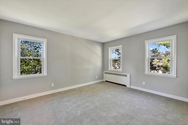 spare room featuring radiator heating unit, plenty of natural light, and light colored carpet