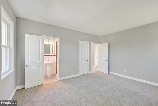 unfurnished bedroom featuring connected bathroom, multiple windows, and light colored carpet