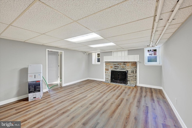 basement featuring a fireplace, a paneled ceiling, light wood-type flooring, and plenty of natural light