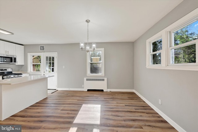 unfurnished dining area with radiator, a healthy amount of sunlight, a chandelier, and dark hardwood / wood-style floors