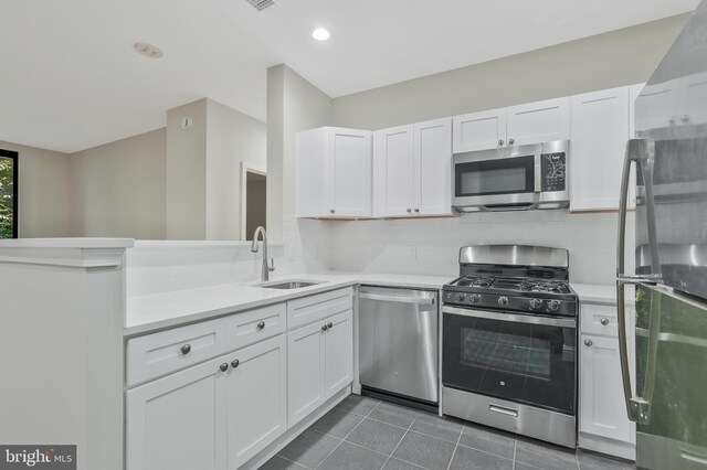 kitchen with tasteful backsplash, appliances with stainless steel finishes, sink, kitchen peninsula, and white cabinetry