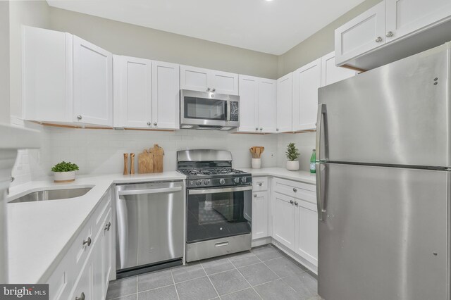 kitchen with appliances with stainless steel finishes, white cabinets, tasteful backsplash, and light tile patterned flooring