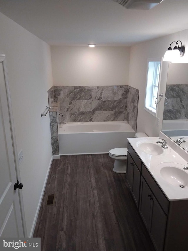 bathroom with wood-type flooring, a bath, vanity, and toilet