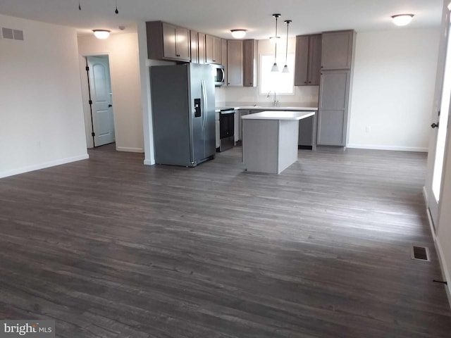 kitchen with appliances with stainless steel finishes, a kitchen island, hanging light fixtures, and dark wood-type flooring