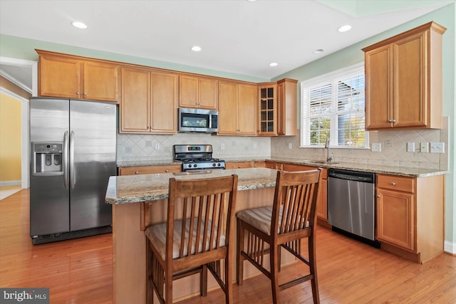 kitchen featuring appliances with stainless steel finishes, a kitchen island, light wood-type flooring, and light stone counters