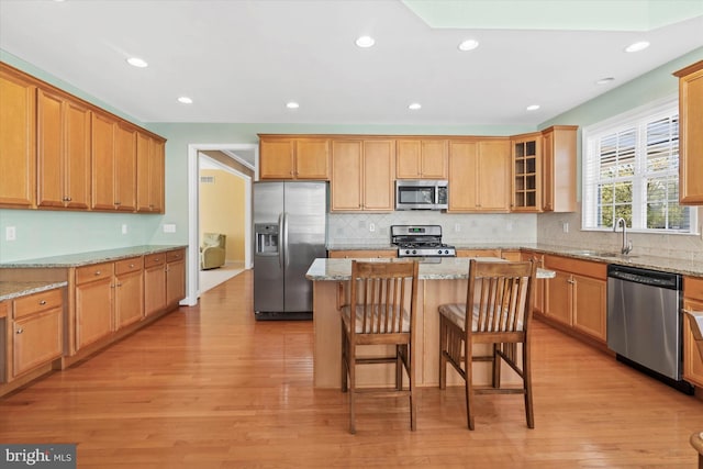 kitchen with a kitchen island, light stone countertops, sink, light hardwood / wood-style floors, and appliances with stainless steel finishes