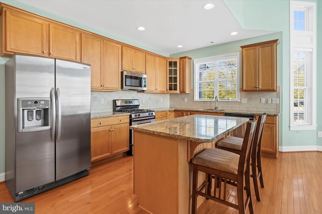 kitchen featuring light wood-type flooring, a kitchen island, light stone counters, decorative backsplash, and appliances with stainless steel finishes