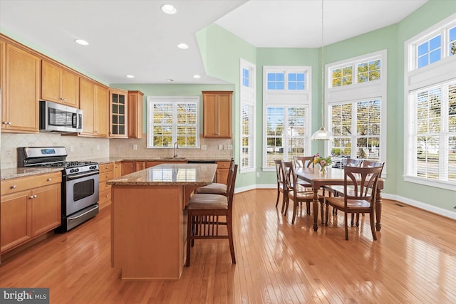 kitchen with light hardwood / wood-style flooring, appliances with stainless steel finishes, light stone countertops, and a center island