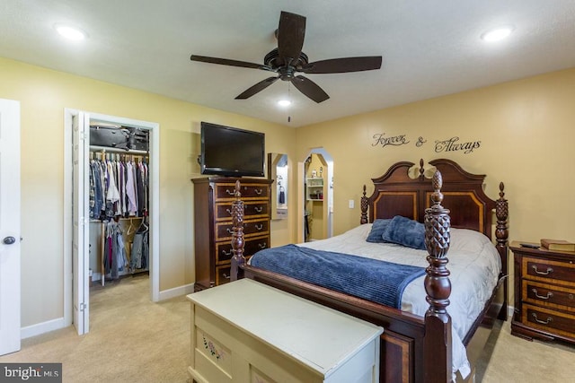 bedroom featuring a spacious closet, a closet, light colored carpet, and ceiling fan