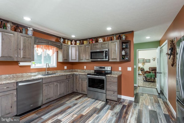 kitchen with stainless steel appliances, light stone countertops, dark wood-type flooring, and sink