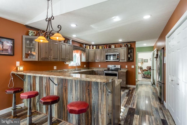 kitchen with stainless steel appliances, dark wood-type flooring, kitchen peninsula, pendant lighting, and a kitchen bar