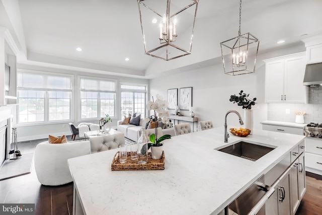 kitchen with light stone counters, a kitchen island with sink, dark wood-type flooring, sink, and pendant lighting