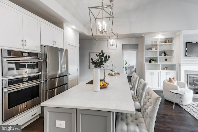 kitchen featuring pendant lighting, a kitchen island with sink, appliances with stainless steel finishes, and dark hardwood / wood-style flooring