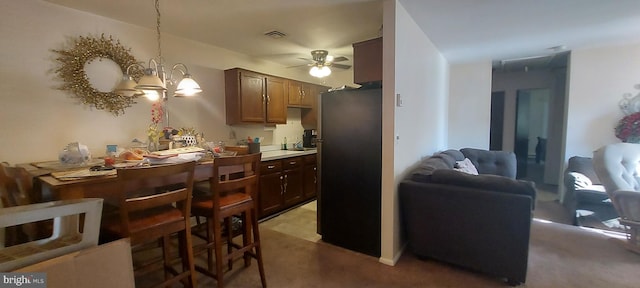 kitchen featuring carpet floors, black refrigerator, ceiling fan with notable chandelier, and pendant lighting