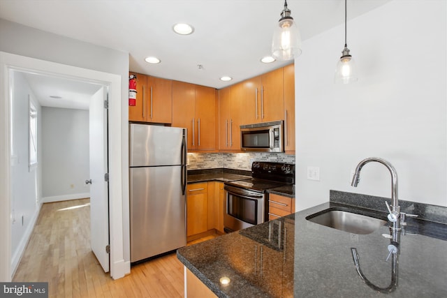 kitchen featuring appliances with stainless steel finishes, sink, light wood-type flooring, hanging light fixtures, and dark stone counters