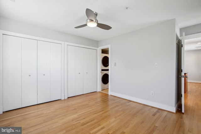 unfurnished bedroom featuring stacked washer and dryer, light hardwood / wood-style flooring, two closets, and ceiling fan