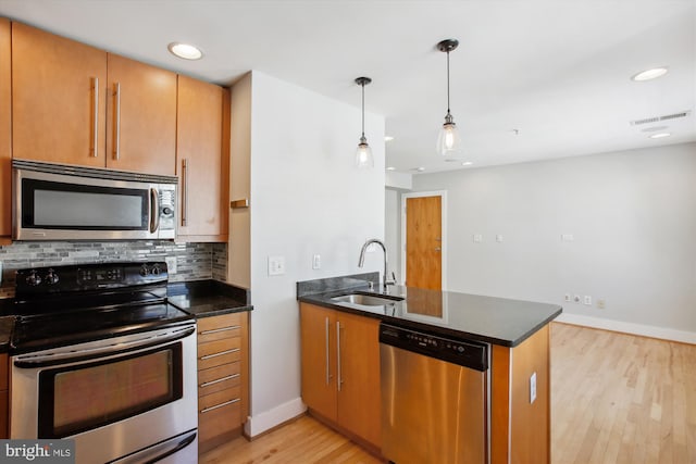 kitchen featuring light hardwood / wood-style floors, appliances with stainless steel finishes, decorative light fixtures, and kitchen peninsula