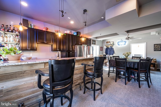 kitchen with stainless steel fridge, ceiling fan, a kitchen bar, pendant lighting, and light stone counters