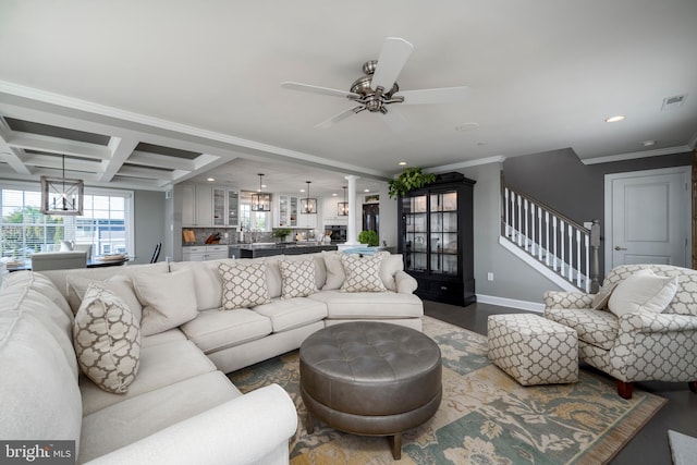 living room with beam ceiling, coffered ceiling, ornamental molding, and ceiling fan with notable chandelier