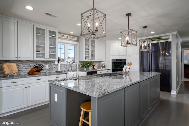 kitchen featuring decorative backsplash, white cabinetry, hanging light fixtures, and a center island with sink