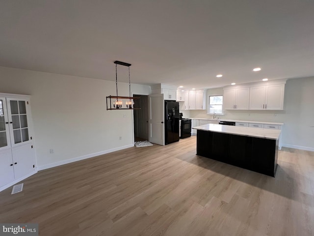 kitchen featuring a kitchen island, hanging light fixtures, black appliances, light wood-type flooring, and white cabinets