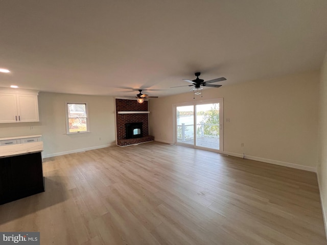 unfurnished living room with light hardwood / wood-style flooring, ceiling fan, a brick fireplace, and a wealth of natural light